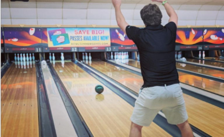 A Cognito Forms employee bowling, with their arms raised, as a bowling ball rolls down the lane.