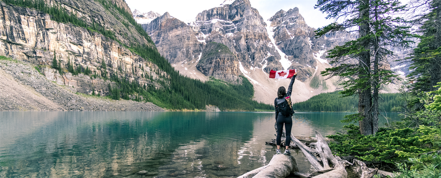 women hiking along a river in the mountains standing on a log holding a Canadian flag