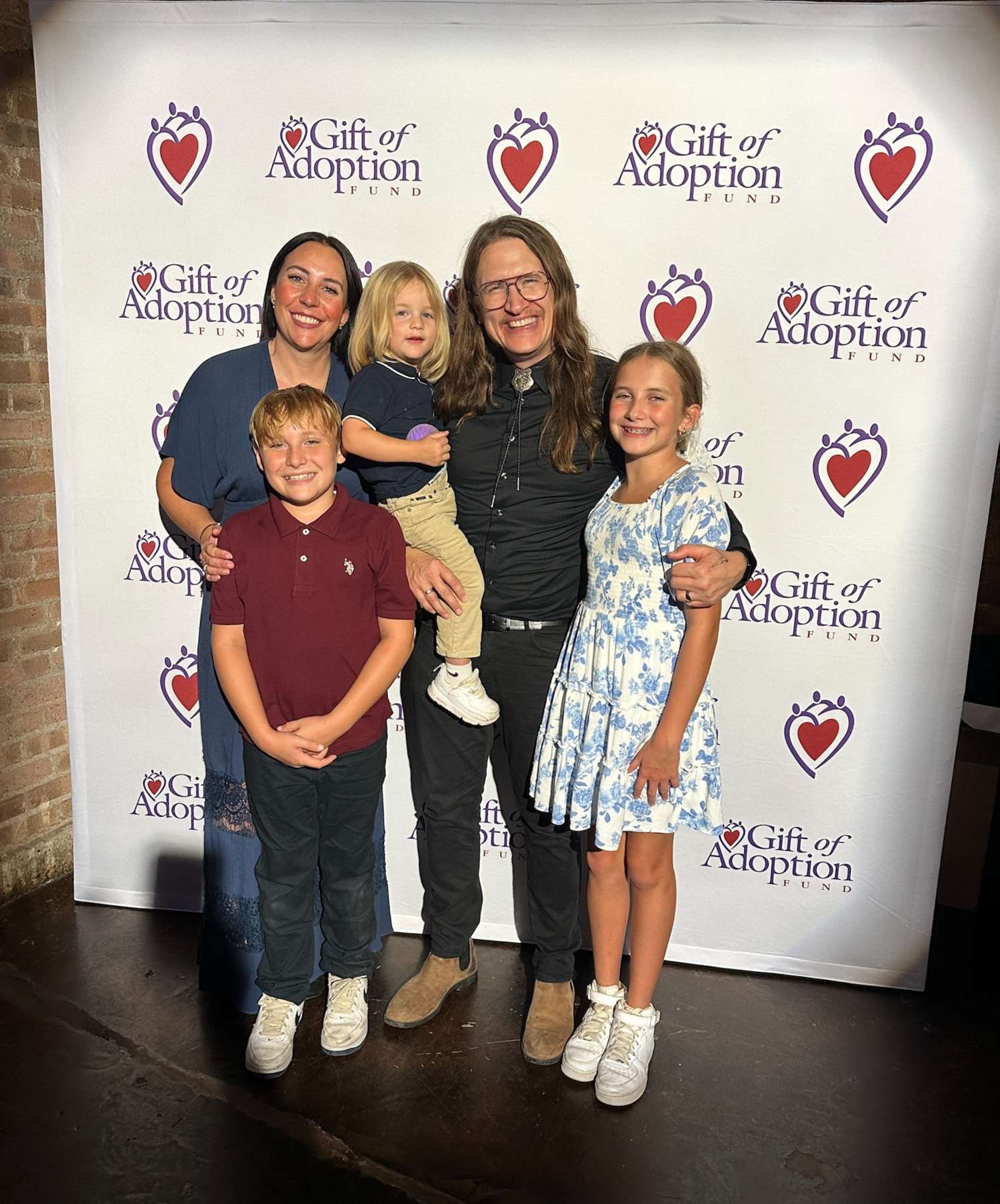 family_photo_in_front_of_Gift_of_Adoption_logo_backdrop.jpg