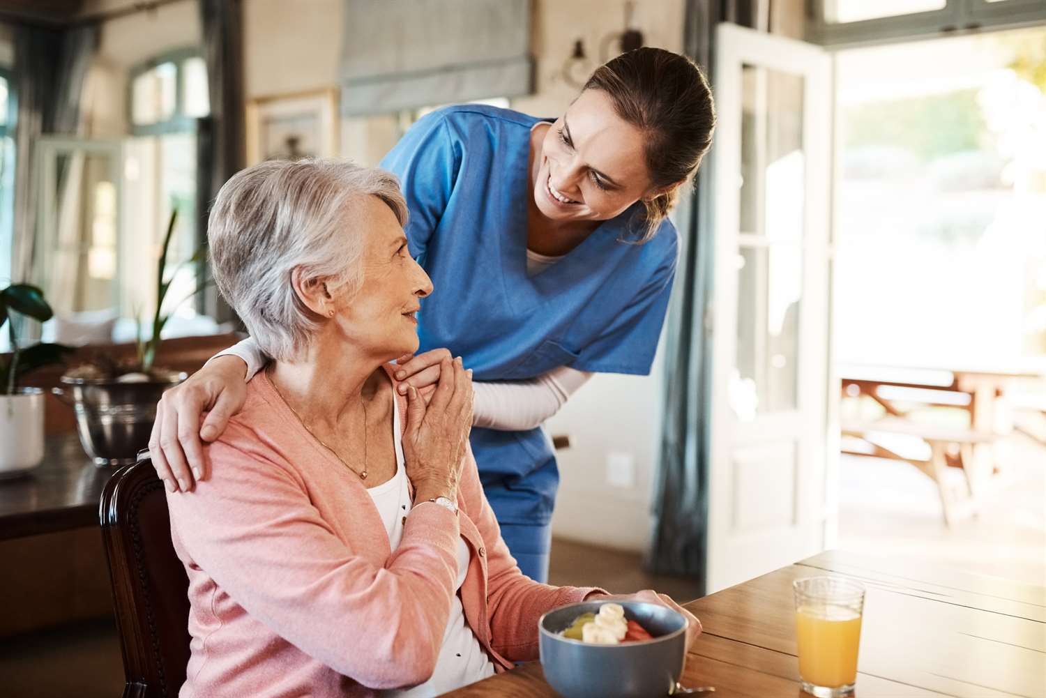 Home care nurse in a blue uniform helping a woman with her breakfast.