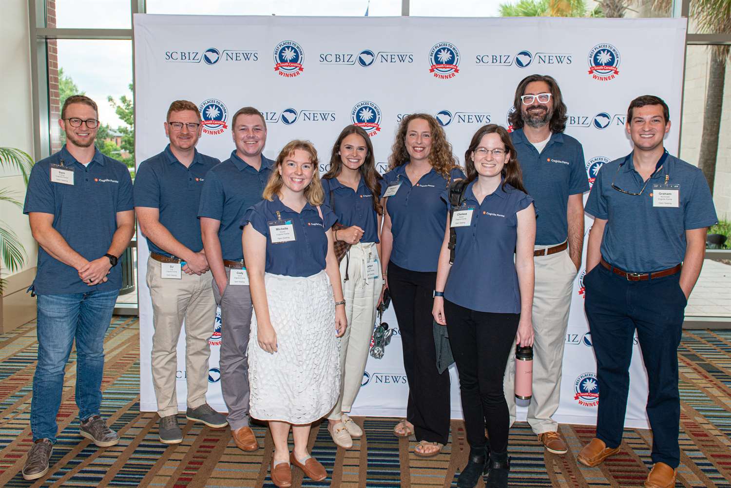 Group photo of the Cognito Forms team with branded shirts in front of a "Best Places to Work in SC" banner.