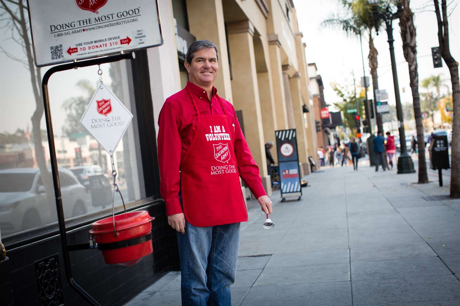 Salvation army red kettle worker standing on sidewalk.