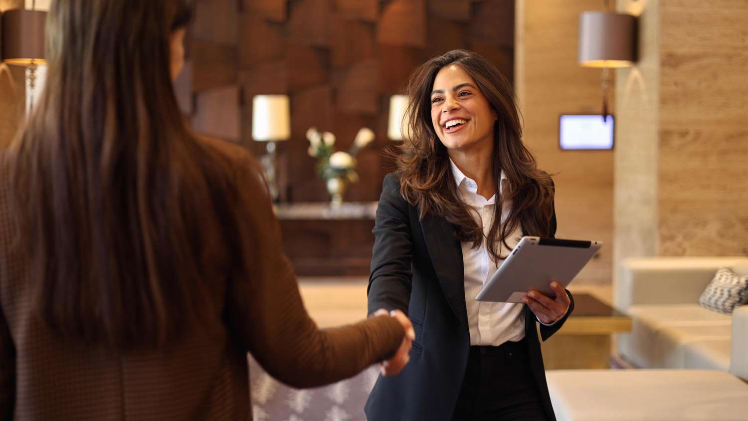 women holding an iPad shaking hands with a traveler in a hotel lobby