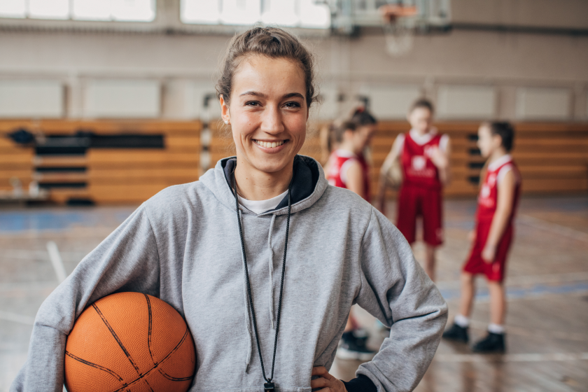 female youth basketball coach holding a basketball in front of team