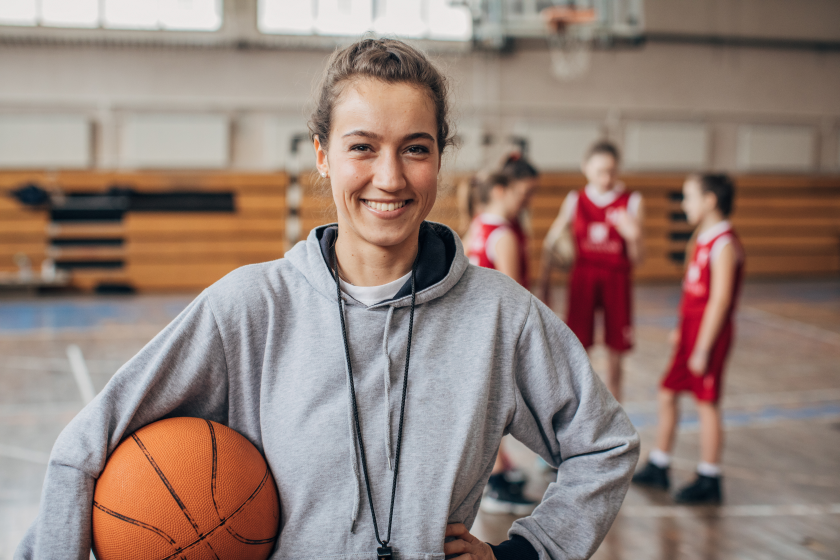 Female basketball coach with team holding a basketball.