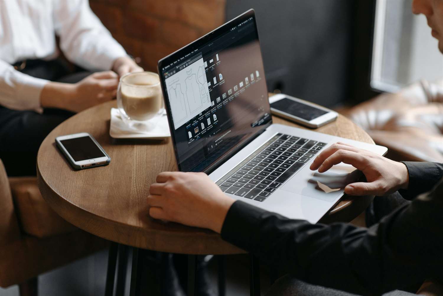 Person filling out information on a laptop and another person at the same table with a cup of coffee