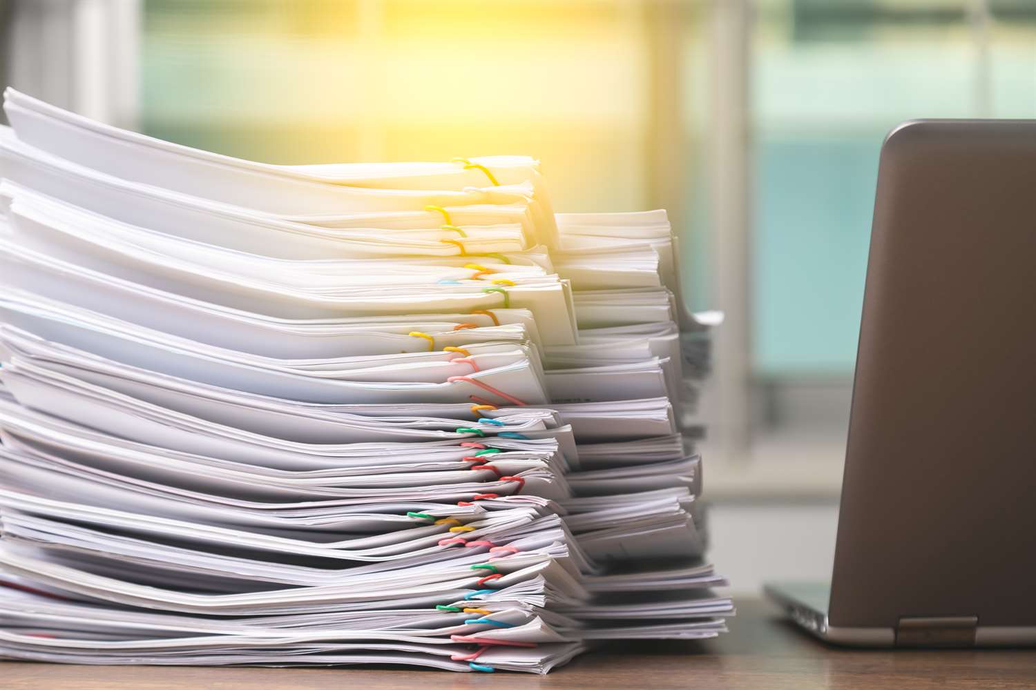 Stack of papers on a desk next to a laptop.