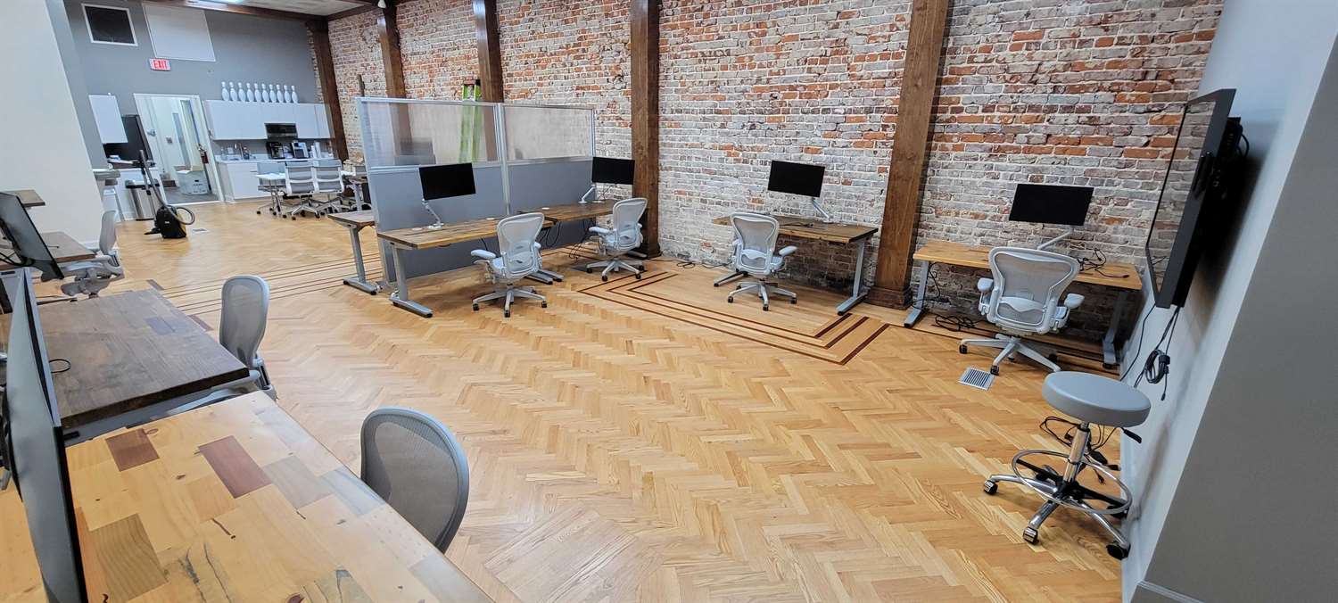 An open-plan office space with brick walls, wooden flooring, and desks equipped with monitors.