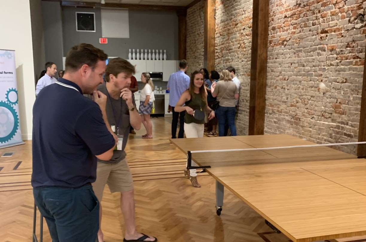 Cognito Forms team members enjoying a casual ping pong game in a brick-walled office space.